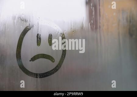 Trauriges Gesicht auf nebligem Fenster, Platz für Text. Regenwetter Stockfoto