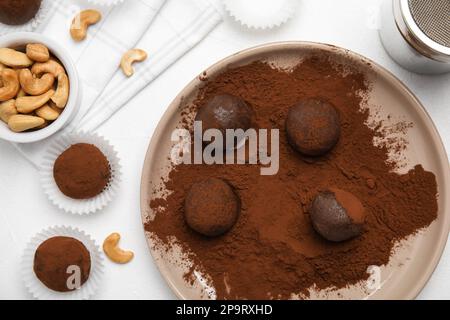 Köstliche Schokoladentrüffel mit Kakaopulver und Nüssen auf einem weißen Tisch, flach liegend Stockfoto