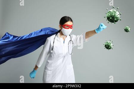 Arzt trägt Gesichtsmaske und Superheldenkostüm Kampf gegen Viren auf hellgrauem Hintergrund Stockfoto