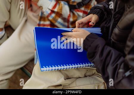 Eine Schülerin öffnet ihr Notizbuch. Sie ist dabei, draußen mit ihrem Freund zu lernen Stockfoto