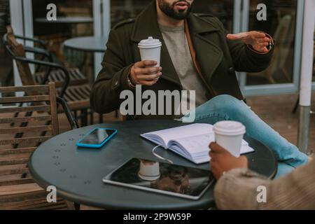Nahaufnahme eines jungen Geschäftsmannes, der mit seinen Händen erklärt und gestikuliert. Er hält eine Tasse Tee Stockfoto