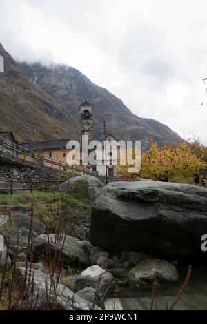 Kirchturm des Dorfes Lavertezzo, Val Verzasca, Schweiz an Berghängen mit bunten Bäumen an einem bewölkten Herbsttag Stockfoto