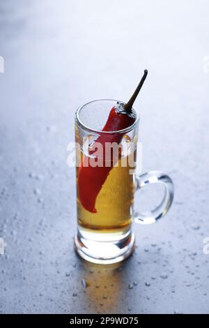 Rote heiße Chili-Paprika und Wodka in Glas auf grauem Tisch Stockfoto