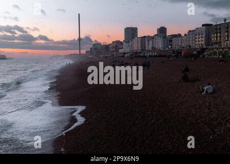 Sonnenuntergang am Brighton Beach im Winter. Viele Leute versammelten sich auf den Kieseln, um den Sonnenuntergang zu beobachten Stockfoto