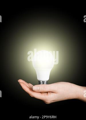 Frauenhand hält LED-Glühbirne auf schwarzem Hintergrund, Energiekonzept Stockfoto