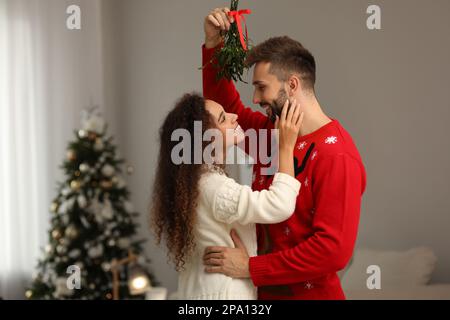 Ein reizendes Paar unter Mistelzweigen im Zimmer, das zu Weihnachten dekoriert war Stockfoto