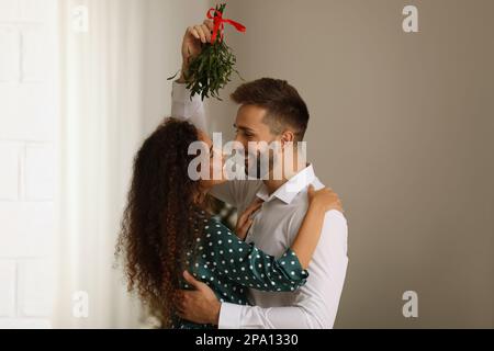 Schönes Paar unter Mistelzweigen im Zimmer. Weihnachtszeit Stockfoto