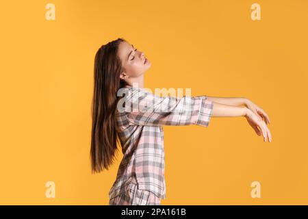 Junge Frau, die Schlafanzüge im Schlafwandlerzustand auf gelbem Hintergrund trägt Stockfoto