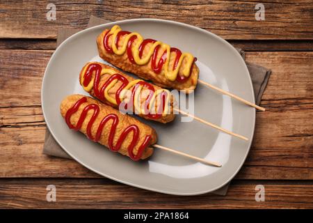 Köstliche Corn Dogs mit Senf und Ketchup auf einem Holztisch, Blick von oben Stockfoto