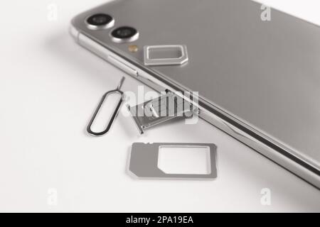 SIM-Karte, Mobiltelefon und Auswerferwerkzeug auf weißem Tisch Stockfoto