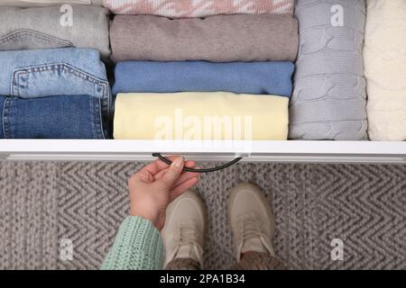 Eine Frau öffnet die Schublade mit gefalteter Kleidung im Innenbereich, Draufsicht. Vertikale Lagerung Stockfoto