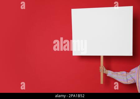 Eine Frau mit einem leeren Schild auf rotem Hintergrund, Nahaufnahme. Platz für Text Stockfoto