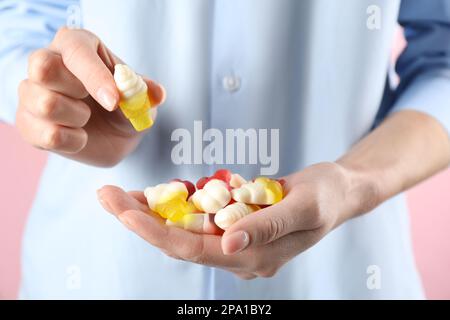 Eine Frau, die eine Handvoll leckerer, gummiiger Eiskegel in Form von Süßigkeiten auf pinkfarbenem Hintergrund hält, Nahaufnahme Stockfoto