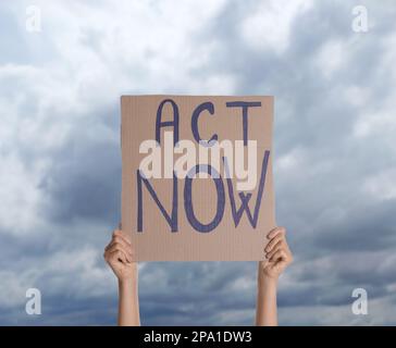 Protestor hält Plakat mit Text Act Now Against Cloudy Sky, Nahaufnahme. Klimaschutz Stockfoto