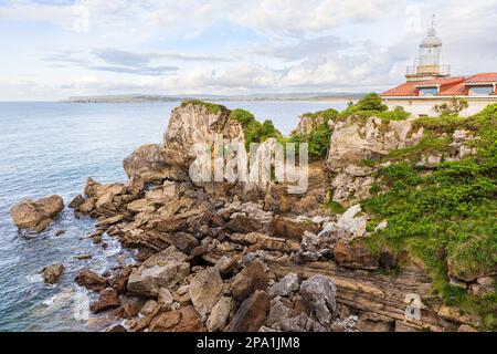 Klippen, teilweise mit Sträuchern bedeckt, Atlantik und Leuchtturm Faro de La Cerda. Magdalena Peninsula, Santander, Kantabrien, Spanien. Stockfoto