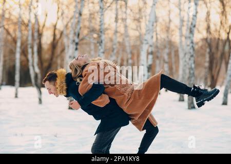 Liebevolles junges Paar, das im Winterwaldpark spielt und Spaß hat. Stockfoto