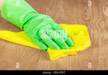 Grüner Handschuh zum Abwischen von Staub vom Holzschreibtisch mit Mikrofasertuch und Wischtuch. Stockfoto