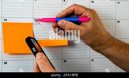 Halten Sie das Telefon in der Hand und markieren Sie das Datum im Kalender mit einem Kopierfeld Stockfoto