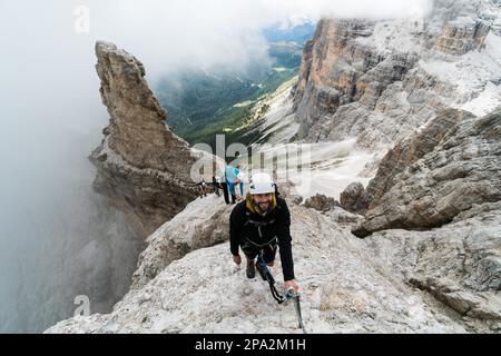 Gruppe junger Bergsteiger auf einer steilen Via Ferrata mit einem grandiosen Blick auf die italienischen Dolomiten in Alta Badia dahinter Stockfoto