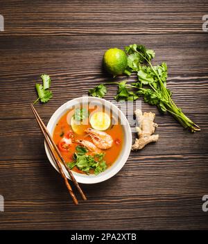 Heiße, frische, würzige traditionelle thailändische Suppe tom Yum mit Garnelen, Limette, Koriander in einer Schüssel auf rustikalem Holzhintergrund, Draufsicht. Authentischer Schweiß und sauer Stockfoto