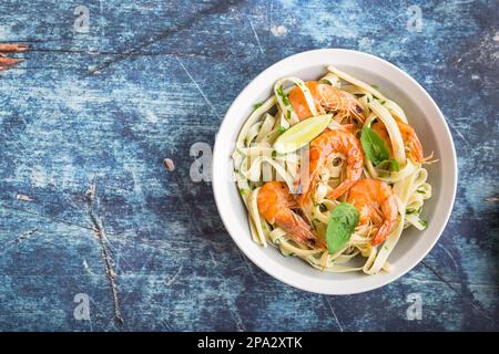 Hausgemachte Pasta mit gebratenen Garnelen und Basilikum auf rustikalem blauem Holzhintergrund. Platz für Text. Pasta mit Meeresfrüchten auf dem Teller. Draufsicht. Nahaufnahme. Stockfoto