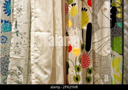 Farbenfrohe Vorhangmuster, die in einem Einzelhandelsgeschäft an Bügeln auf einer Schiene hängen. Im Laden hängende Stoffvorhänge - Textil Stockfoto