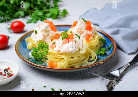 Nudelgerichte mit Lachs, cremiger Sauce und rotem Kaviar auf einem Teller, frisch zubereitete Pasta, leckeres Essen Stockfoto