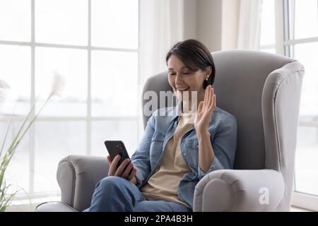 Fröhliche, glückliche, reife Handybenutzerin, die mit der Grußhand hallo winkt Stockfoto