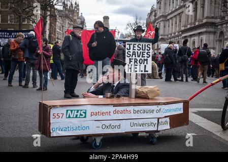 London, Großbritannien, 11. März 2023. Ein Protest und marsch gipfelten vor der Downing Street, London. Der Marsch sollte auf mangelnde Investitionen in den britischen NHS und die aktuelle NHS-Krise hinweisen. Zu den Rednern zählte Jeremy Corbyn, ehemaliger Labour-Führer, und es gab eine starke Gewerkschaftsvertretung. Hier sitzt ein Mann mit Hut und isst seine Sandwiches neben einem Dummy-Sarg, während ein religiöser Aktivister versucht, Demonstranten aus der Hölle zu retten. #SOSNHSDEMO (Tennessee Jones - Alamy Live News) Stockfoto