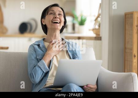 Aufgeregte ältere Dame im Ruhestand, die über ihren Laptop lacht Stockfoto