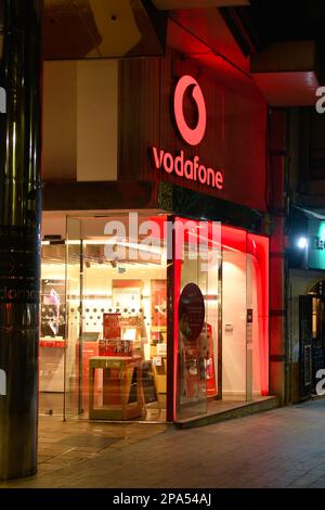 Beleuchtetes Business-Schild oder Logo in einem Geschäft oder Geschäft in Vodafone. Szene der Stadt Alicante bei Nacht in Spanien. Stockfoto