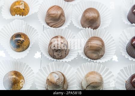 Ein Schokoladenkonfekt und Backglas mit handgefertigten individuellen Trüffeln in verschiedenen Farben und Geschmacksrichtungen mit weißen Papierverpackungen Stockfoto
