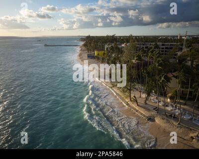 Schüsse von einer Drohne. Ein gemütliches Resort am Meer. Sauberer Sandstrand, tropische Pflanzen, türkisfarbenes Meerwasser und weiße schaumige Wellen. Wolkiger Himmel. Stockfoto