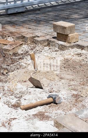 Eine Kelle im Sand neben einem kleinen Hammer und Betonblöcken an einem sonnigen Tag vertikal. Stockfoto