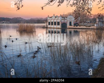 Die ruhige Schönheit des Banyoles Lake spiegelt sich in der Dämmerung am Himmel wider, eingerahmt von einem majestätischen Bauwerk und umgeben von Bäumen. Stockfoto