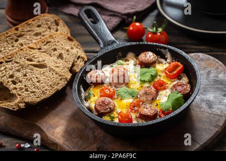 Spiegeleier mit würzigen Würstchen in einer gusseisernen Bratpfanne und Brot im rustikalen Stil Stockfoto