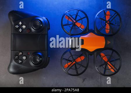 Spiele die orangefarbene Mini-Drohne auf dunklem Hintergrund und kontrolliere sie von einem Gamepad aus Stockfoto