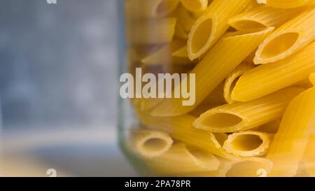 Nudelpenne in Glasgefäß, Nahaufnahme von rohen Speisen mit selektivem Fokus und verschwommenem Hintergrund Stockfoto