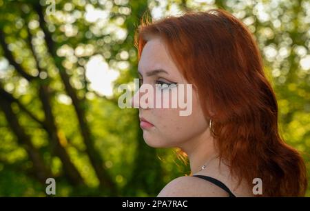 Porträt eines jungen, hübschen rothaarigen Mädchens im Profil, in grüner Natur Stockfoto