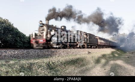 Dampflokomotive mit Touristenbussen schließt Bewegungsunschärfe auf Bahngleisen auf Landstraßen ab. Stockfoto