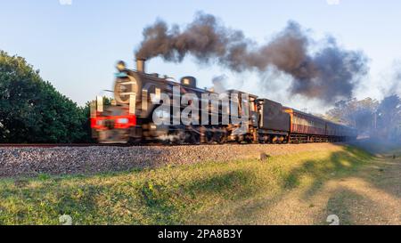 Dampflokomotive mit Touristenbussen schließt Bewegungsunschärfe auf Bahngleisen auf Landstraßen ab. Stockfoto