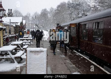 Passagiere, die in einem Schneesturm während der Steam Gala Worth Valley im März 2023 am Bahnhof Oxenhope in den Dampfeisenbahn steigen und ihn verlassen Stockfoto