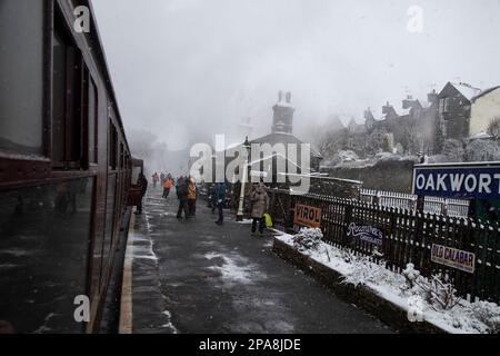 Dampf- und Schneewolken am Bahnhof von Oakworth, während die Passagiere während der Steam Gala Week in die Worth Valley Heritage Railway einsteigen und abfahren Stockfoto