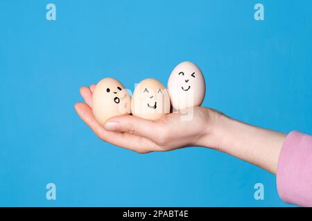 Eine Hand, die drei ostereier hält, mit einem komischen Gesicht drauf. Ostern oder gesunde Ernährung Konzept Stockfoto