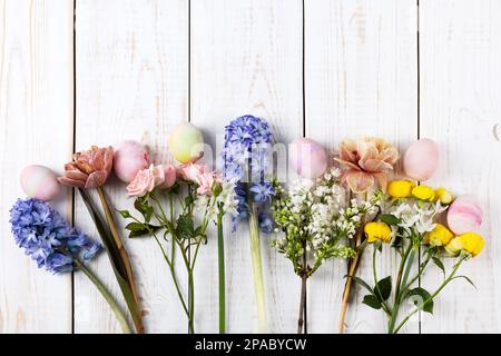 Frühlingsstrauß aus Narzissen, Hyazinthen, Rosen, Tulpen mit bunten ostereiern auf weißem Holzhintergrund. Frohes Osterkonzept. Grußkarte, Bulle Stockfoto