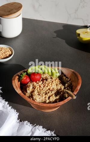 Vegane, hausgemachte Haferflocken in einer Holzschüssel mit Früchten auf einem grauen Tisch Stockfoto