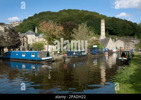 Narrowboats auf dem Rochdale Canal an Hebden Bridge mit der ehemaligen Schornstein der Crossley Mühle in der Ferne, West Yorkshire Stockfoto