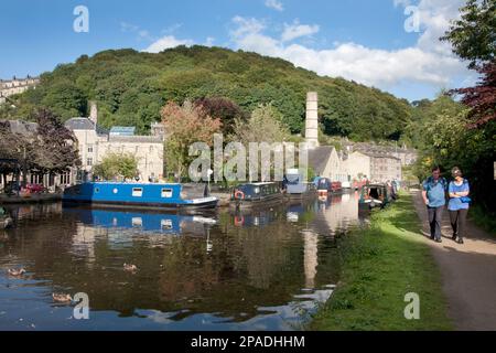 Narrowboats auf dem Rochdale Canal an Hebden Bridge mit der ehemaligen Schornstein der Crossley Mühle in der Ferne, West Yorkshire Stockfoto