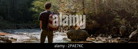 Rückansicht eines Wanderers mit Rucksack, der am Fluss mit Felsen steht und die Natur genießt. Stockfoto