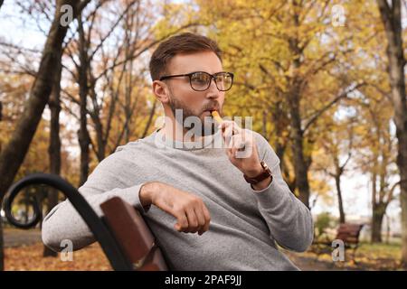 Ein gutaussehender junger Mann, der am Herbsttag im Park elektronische Einwegzigaretten benutzt Stockfoto